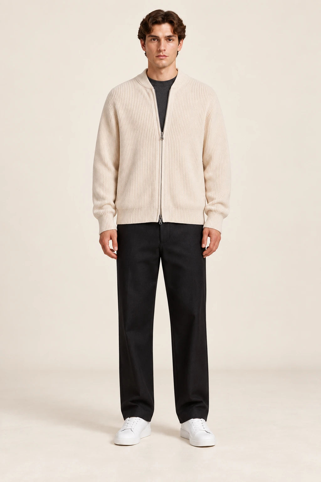 Cardigan beige en maille côtelée fine avec col court et fermeture zippée à double curseur, porté de face dans le studio IVAREE.