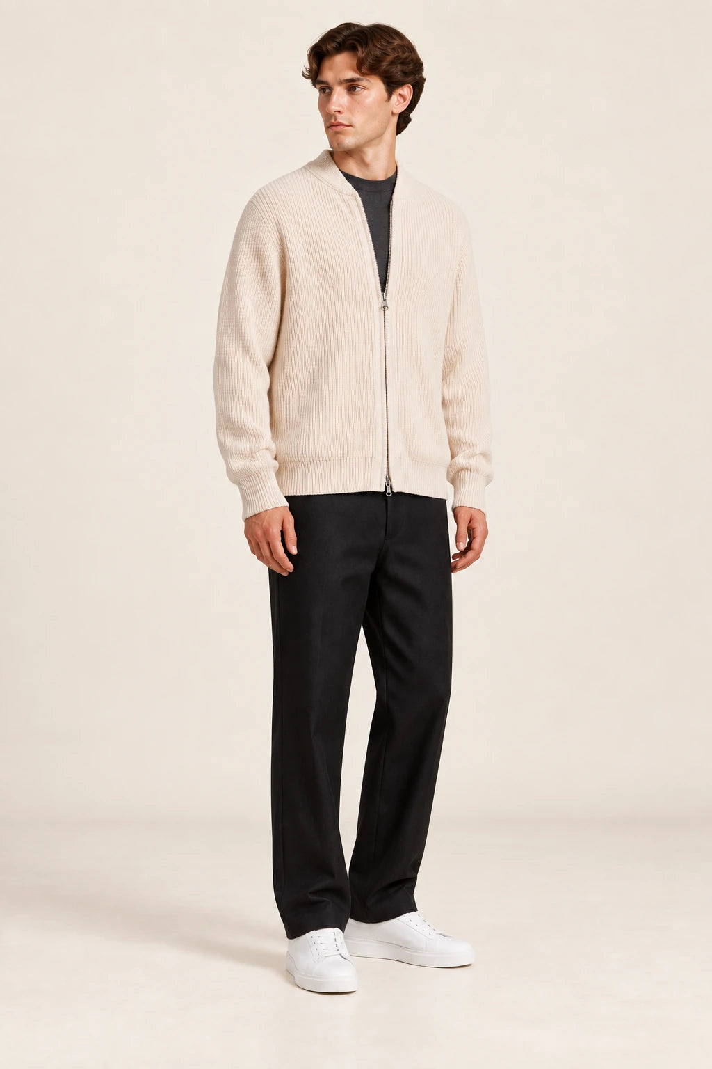Cardigan beige en maille côtelée fine avec fermeture zippée, porté de trois-quarts dans le studio IVAREE.