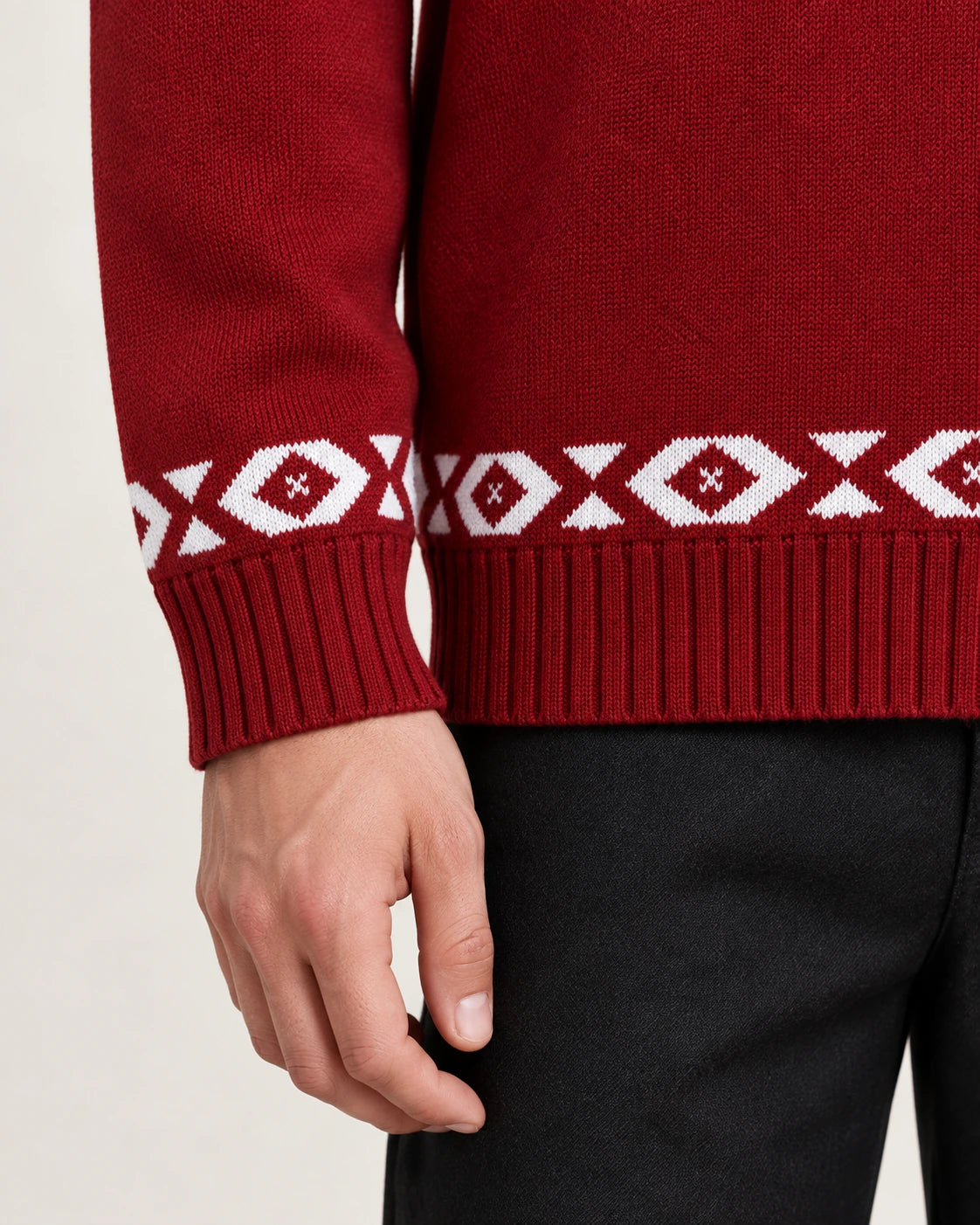 Détail du poignet côtelé et de la bande géométrique blanche du cardigan rouge en maille.