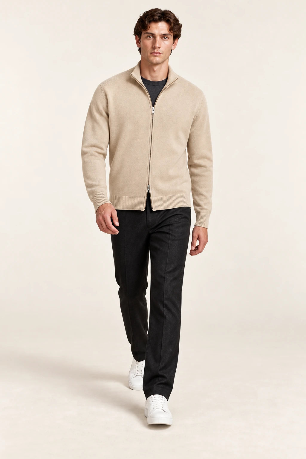 Cardigan beige en maille fine coupe slim avec fermeture zippée, porté en marche de trois-quarts dans le studio IVAREE.