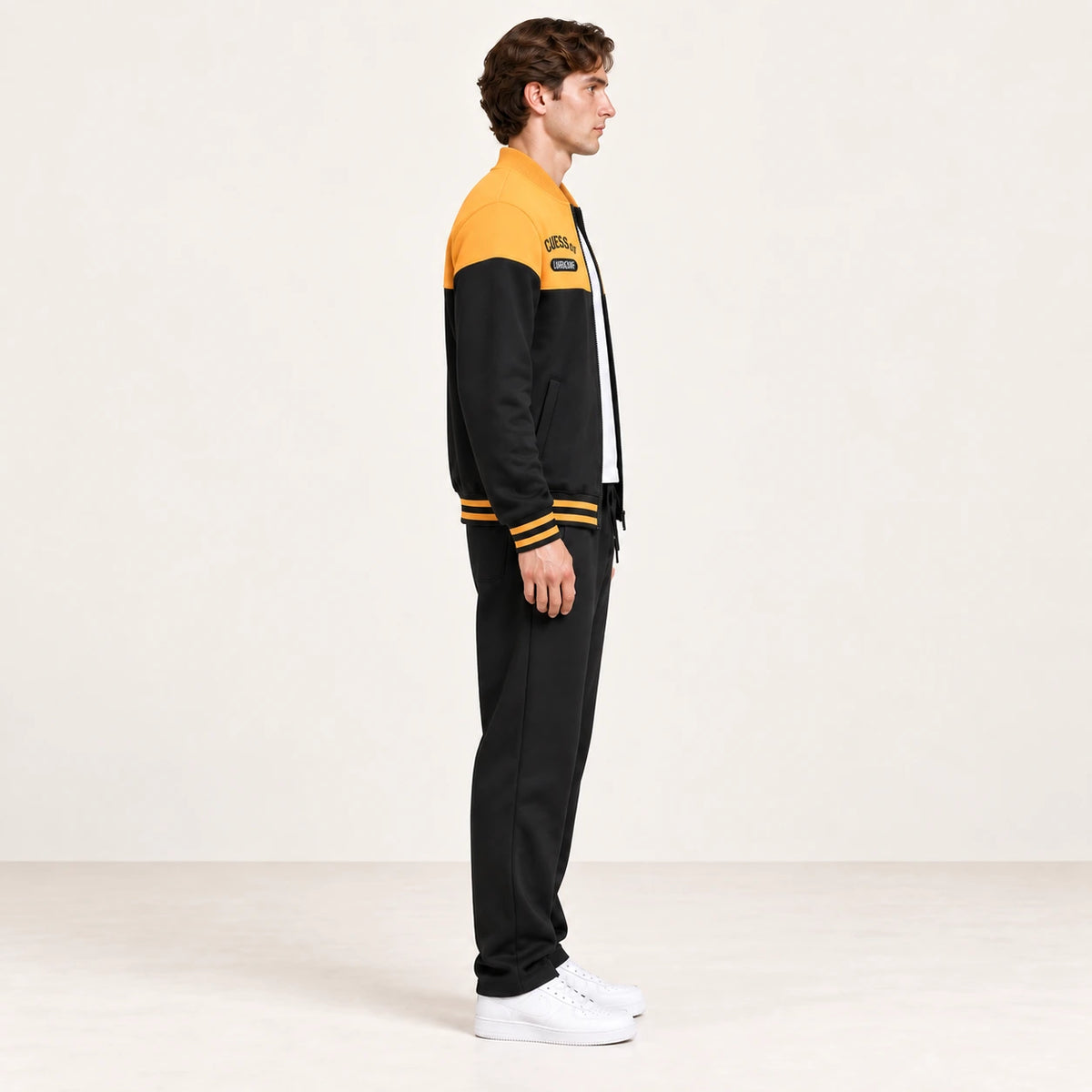 Ensemble de survêtement esprit baseball jaune et noir, porté de profil en studio ivoire