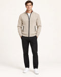 Gilet beige en maille fine avec col montant, fermeture centrale et deux poches zippées, porté de face dans le studio IVAREE.