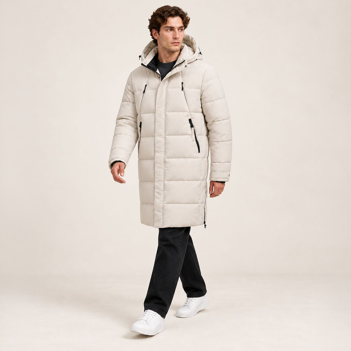 Parka longue beige matelassée à capuche et quatre poches zippées, portée en marche dans le studio IVAREE, format carré 1:1.
