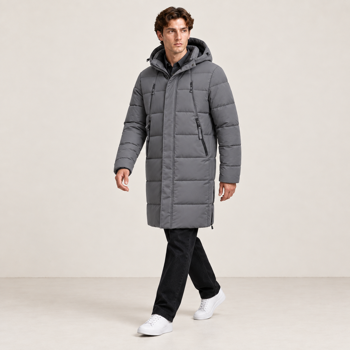 Parka longue grise matelassée à capuche et quatre poches zippées, portée en marche dans le studio IVAREE, format carré 1:1.