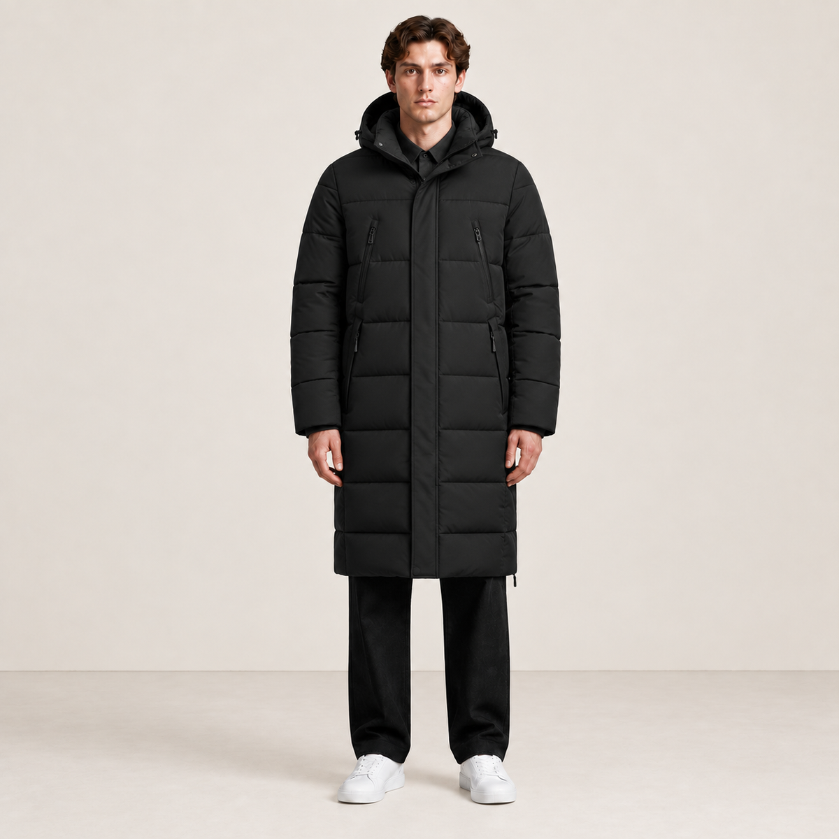 Parka longue noire matelassée à capuche et quatre poches zippées, vue de face dans le studio IVAREE, format carré 1:1.