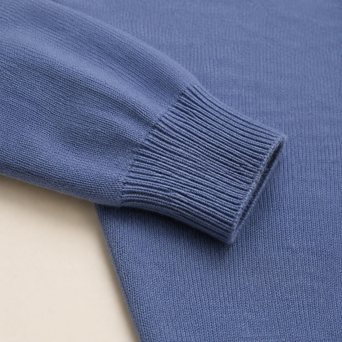 Détail du poignet côtelé et de la maille unie du pull col polo bleu.