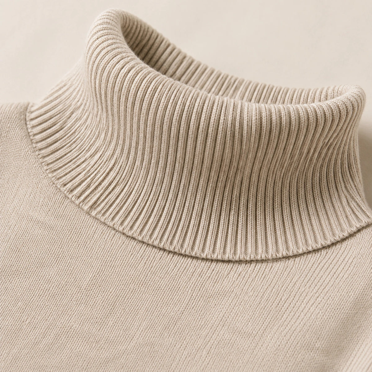 Détail du col roulé côtelé du pull beige en maille fine.