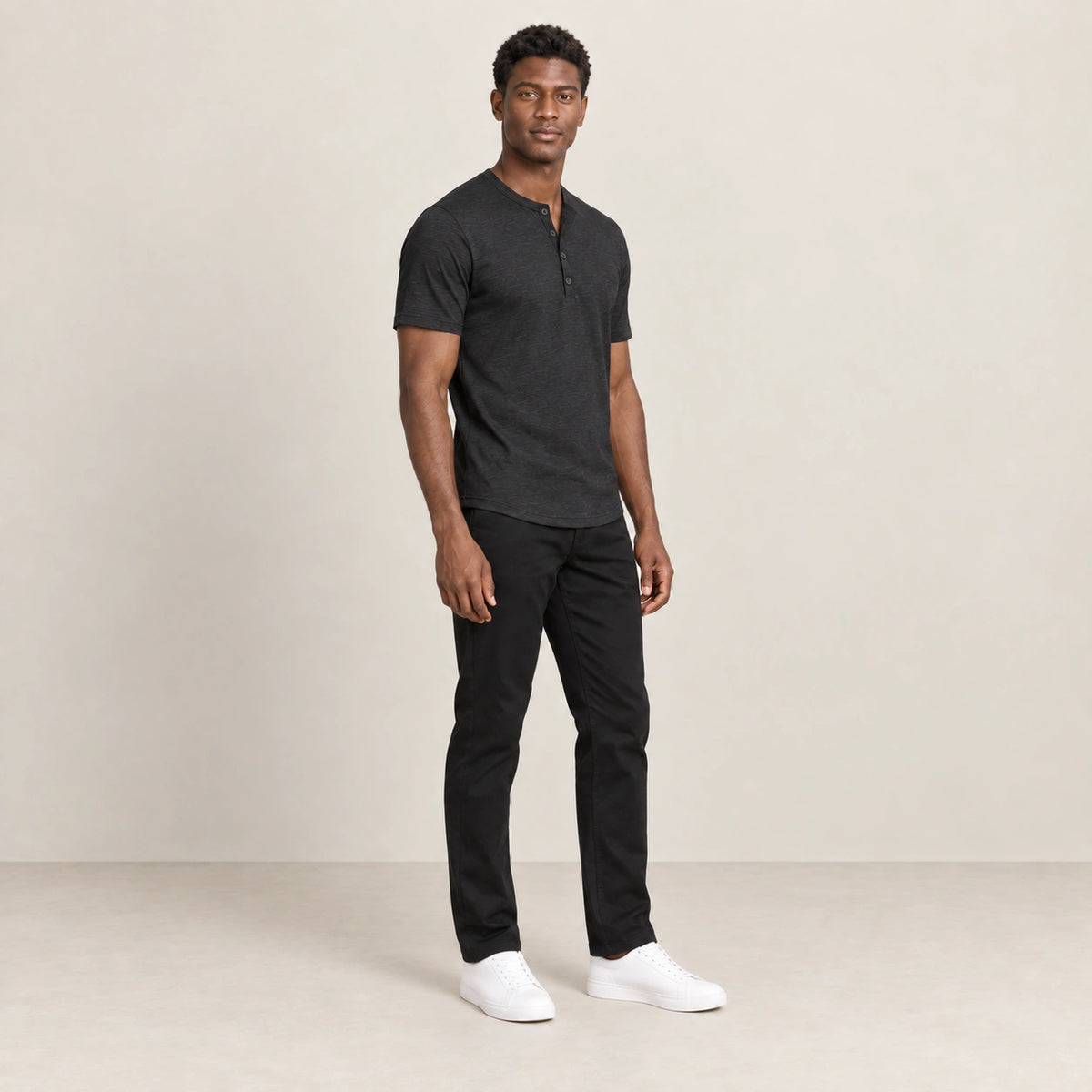 T-shirt noir à col Henley boutonné, porté de trois-quarts dans le studio IVAREE.