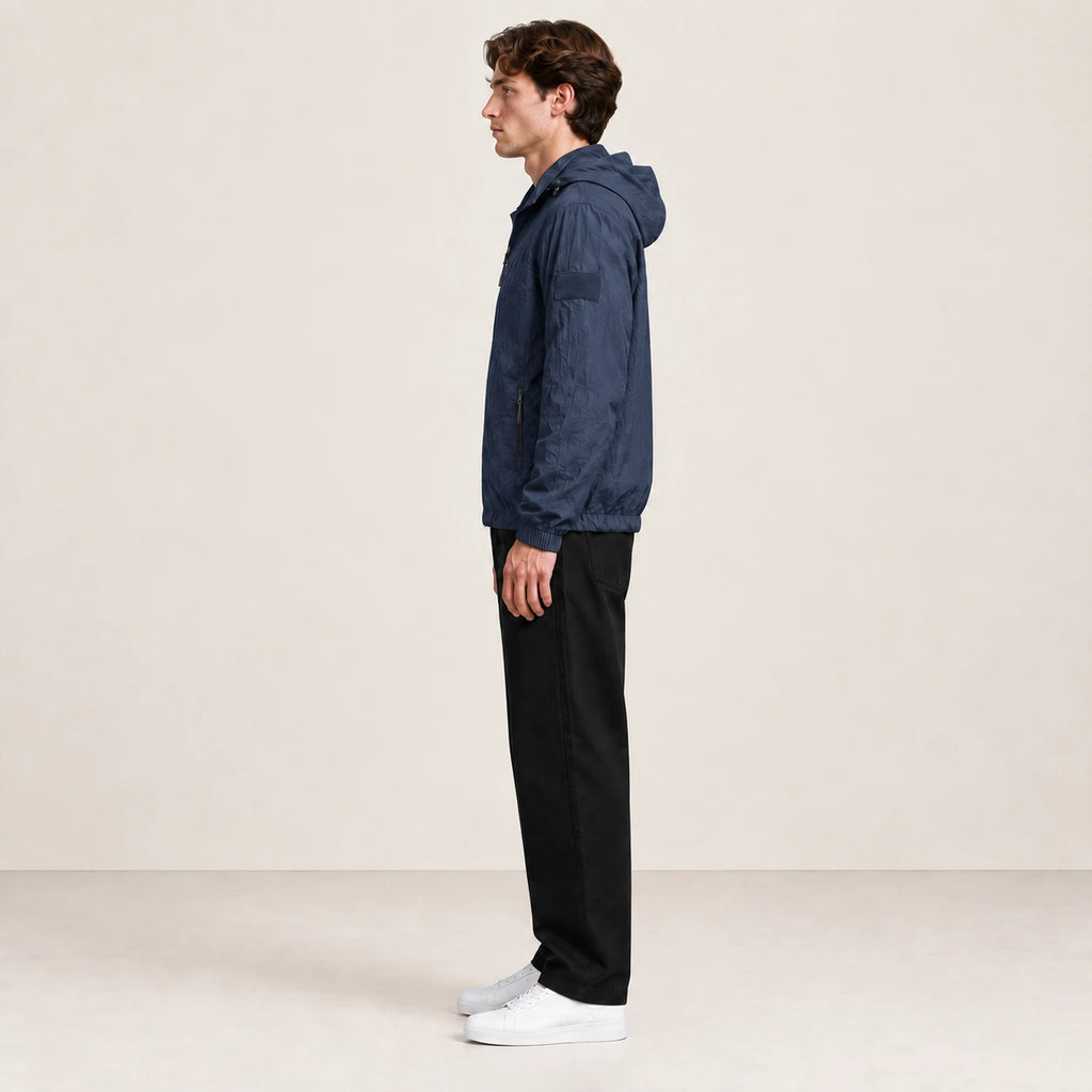 Veste légère bleu marine à capuche et fermeture zippée, portée de profil dans le studio IVAREE.