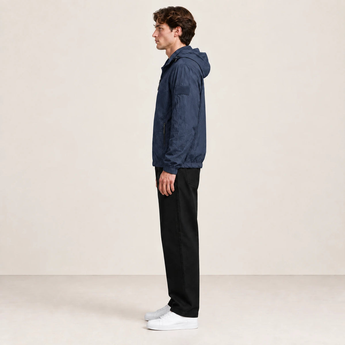 Veste légère bleu marine à capuche et fermeture zippée, portée de profil dans le studio IVAREE.