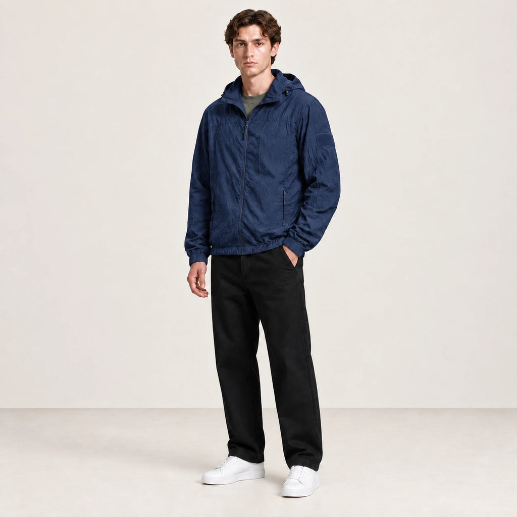 Veste légère bleu marine à capuche et fermeture zippée, portée de trois-quarts dans le studio IVAREE.