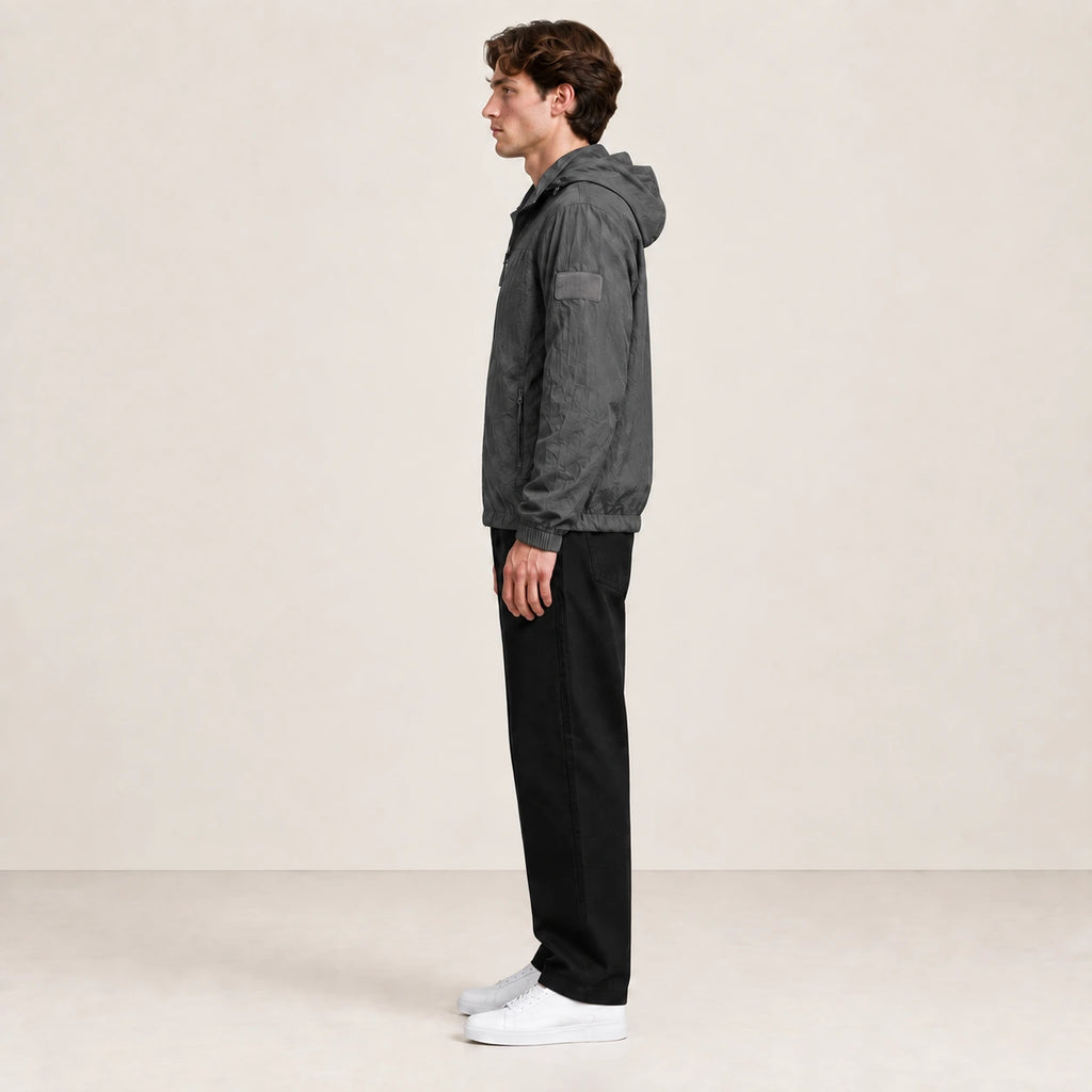 Veste légère gris anthracite à capuche et fermeture zippée, portée de profil dans le studio IVAREE.