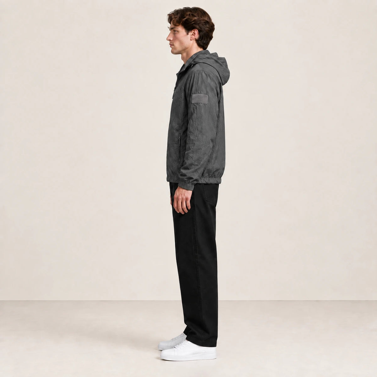 Veste légère gris anthracite à capuche et fermeture zippée, portée de profil dans le studio IVAREE.