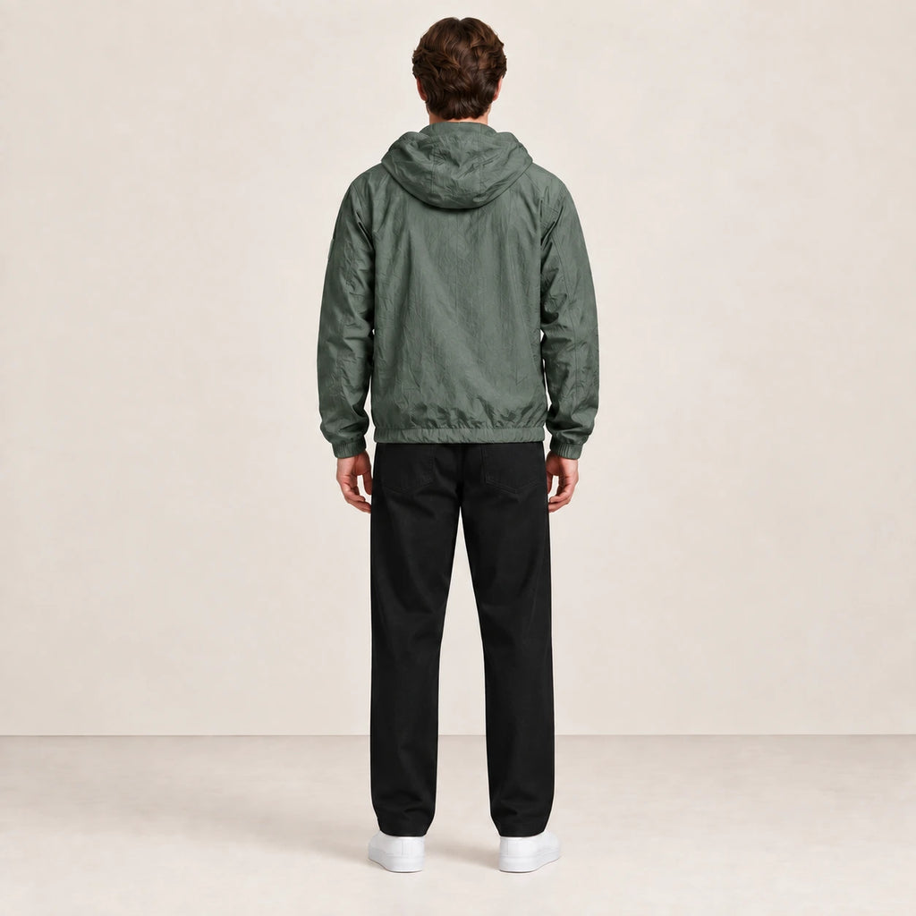 Veste légère vert grisé à capuche, portée de dos dans le studio IVAREE.