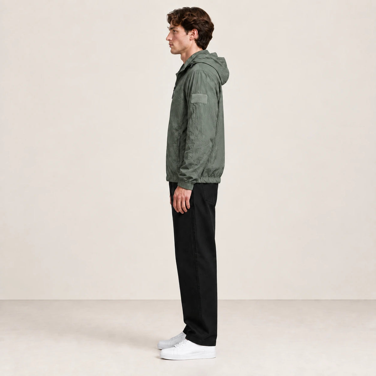 Veste légère vert grisé à capuche et fermeture zippée, portée de profil dans le studio IVAREE.
